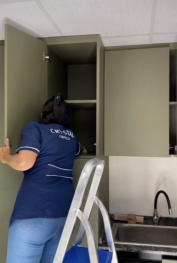 Operaria de Crystal con uniforme azul limpiando los muebles de una cocina